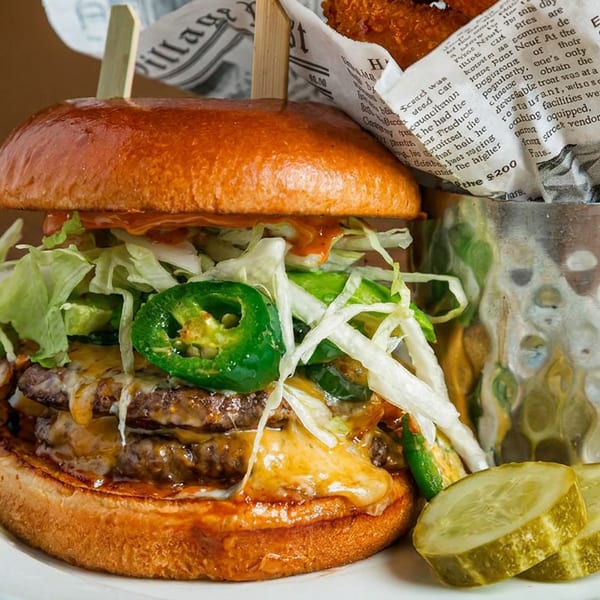 Double cheeseburger with jalapeños, lettuce, pickles, and fries in a metal cup.
