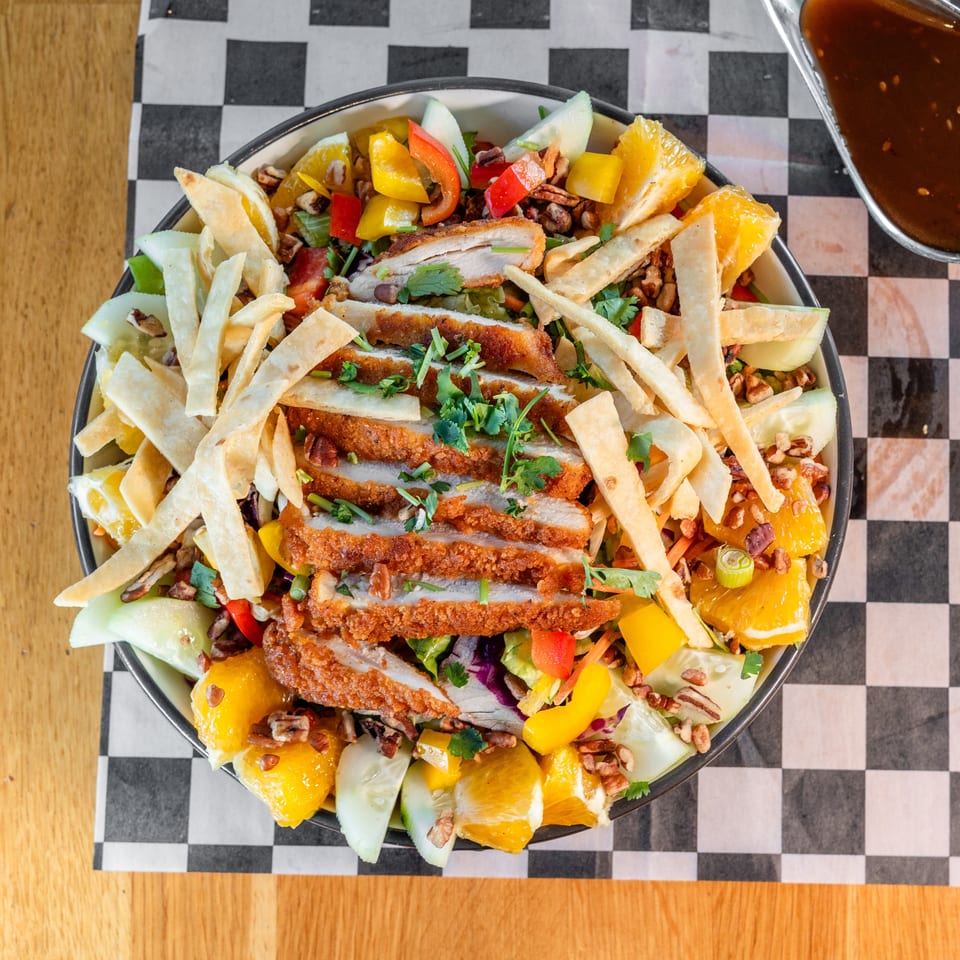 Overhead view of a vibrant salad with fried chicken, oranges, bell peppers, and tortilla strips.