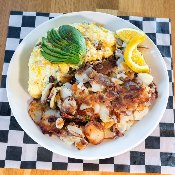 A breakfast plate with an omelet topped with avocado, home fries, and an orange slice.