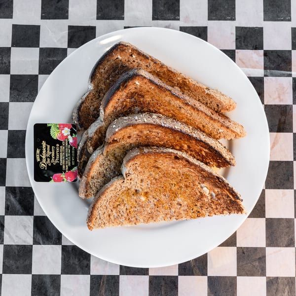 A white plate of buttered toast slices with a small packet of Dickinson's strawberry preserves.