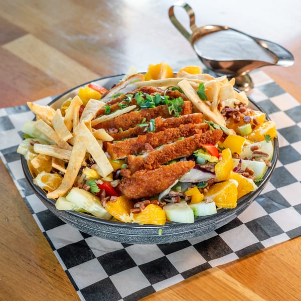 Crispy chicken salad with oranges, cucumbers, nuts, and tortilla strips, with a gravy boat.