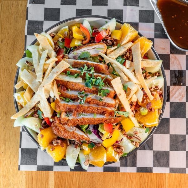 Overhead view of a vibrant salad with crispy chicken, oranges, bell peppers, and tortilla strips.