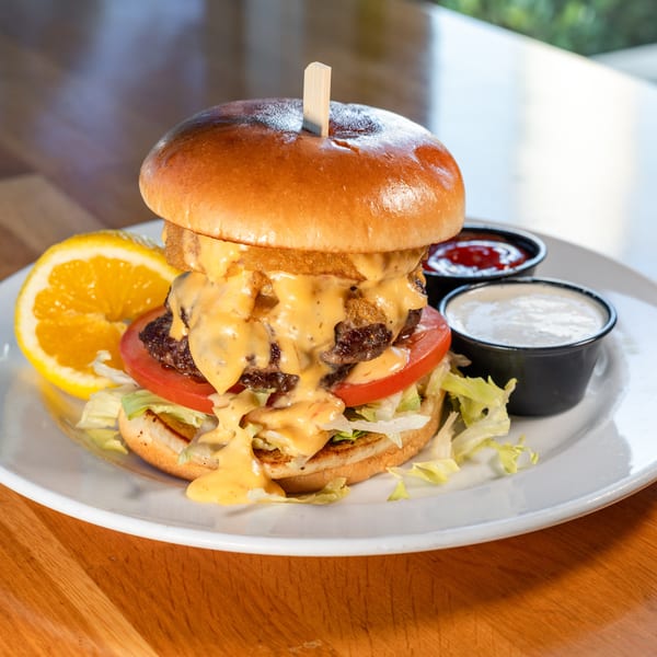 A double cheeseburger with onion rings, melted cheese, lettuce, tomato, and an orange slice.